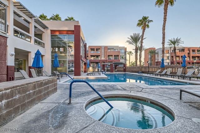 pool at dusk featuring a patio and a community hot tub