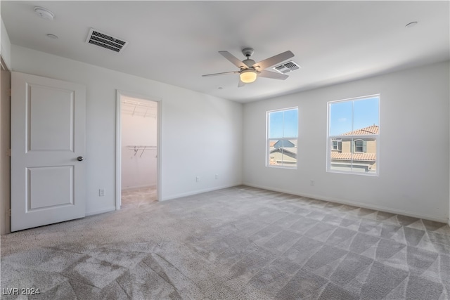 unfurnished bedroom with ceiling fan, light colored carpet, a walk in closet, and a closet