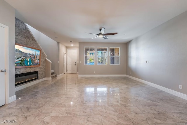 unfurnished living room with a large fireplace, marble finish floor, a ceiling fan, and baseboards