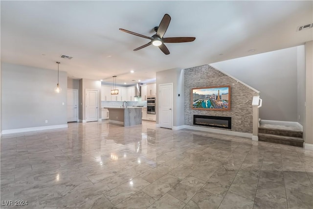 unfurnished living room featuring ceiling fan, a stone fireplace, and sink