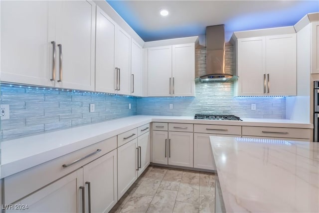 kitchen with backsplash, white cabinets, wall chimney range hood, appliances with stainless steel finishes, and light stone counters