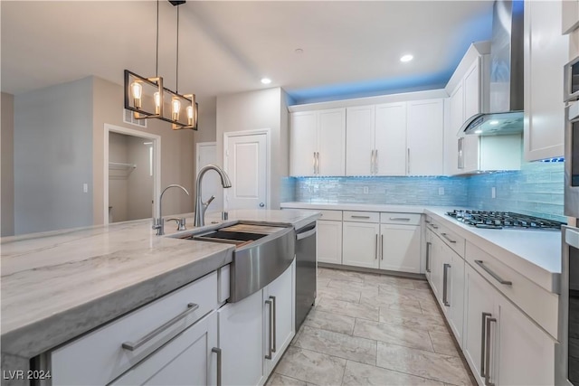 kitchen featuring white cabinets, appliances with stainless steel finishes, hanging light fixtures, wall chimney range hood, and a sink