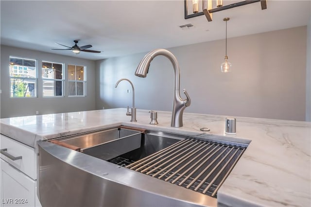 kitchen featuring ceiling fan, sink, light stone countertops, decorative light fixtures, and white cabinets