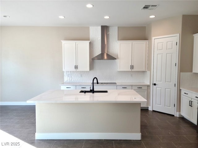 kitchen with a center island with sink, white cabinetry, light stone counters, and wall chimney range hood