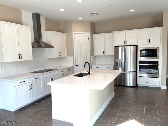 kitchen featuring a kitchen island with sink, white cabinets, wall chimney range hood, sink, and stainless steel appliances