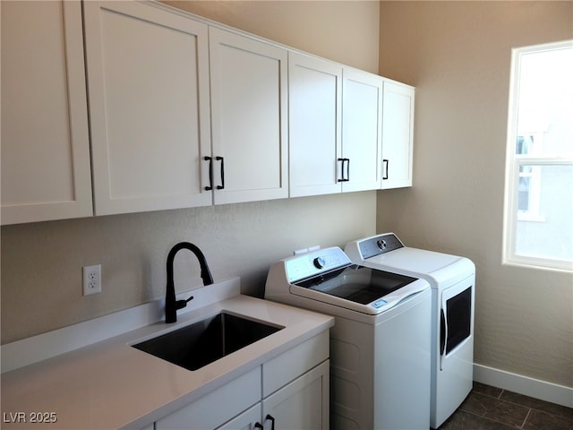 clothes washing area with cabinets, washing machine and clothes dryer, dark tile patterned floors, and sink