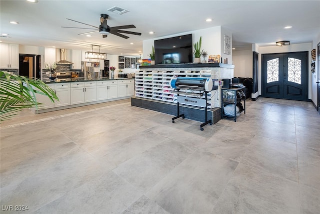 kitchen featuring ceiling fan, white cabinets, hanging light fixtures, and wall chimney range hood