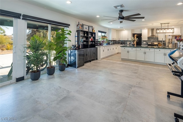 kitchen with a wealth of natural light, white cabinets, hanging light fixtures, and wall chimney range hood