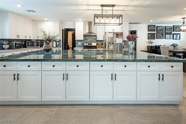 kitchen featuring white cabinetry, wall chimney exhaust hood, hanging light fixtures, and appliances with stainless steel finishes