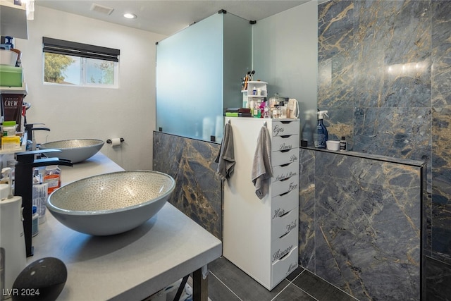 bathroom with walk in shower, tile patterned floors, tile walls, and dual sinks