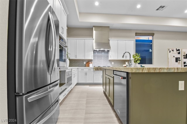 kitchen featuring tasteful backsplash, wall chimney exhaust hood, a kitchen island with sink, white cabinets, and stainless steel fridge