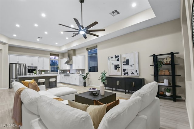 living room with ceiling fan, sink, light wood-type flooring, and a tray ceiling