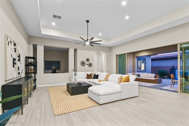 living room featuring light hardwood / wood-style floors, ceiling fan, and a raised ceiling