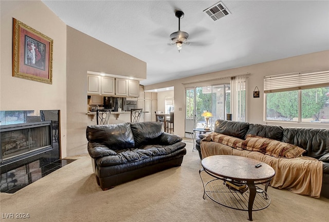 living room with a textured ceiling, vaulted ceiling, a tiled fireplace, light colored carpet, and ceiling fan