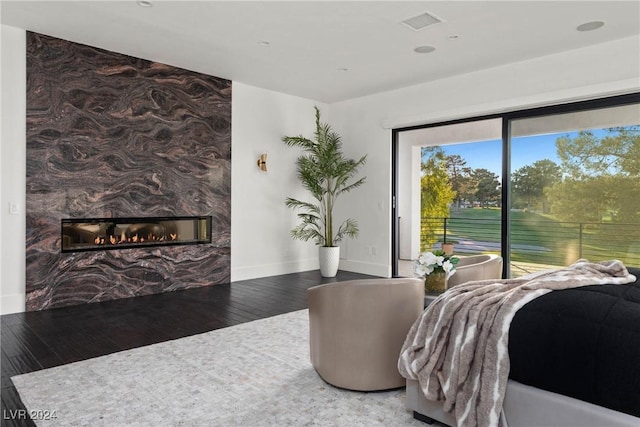 bedroom with access to exterior, visible vents, a large fireplace, wood finished floors, and baseboards