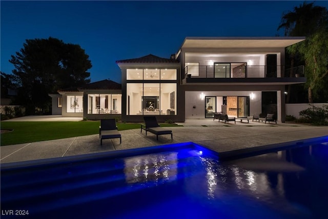 back of house at twilight featuring a balcony, a patio area, a fenced in pool, and stucco siding