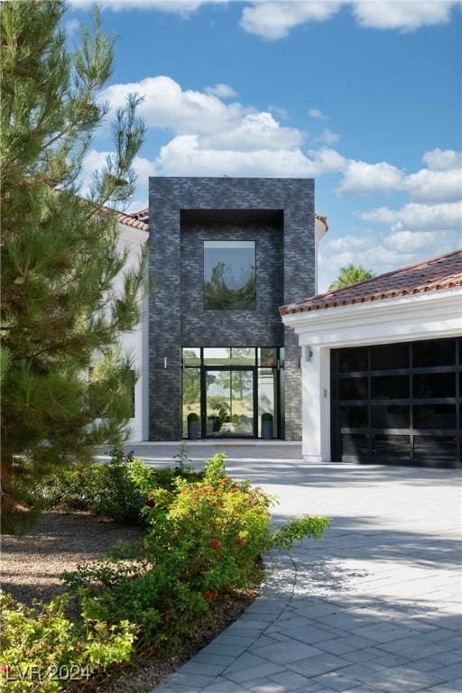 property entrance with driveway, a tiled roof, and an attached garage