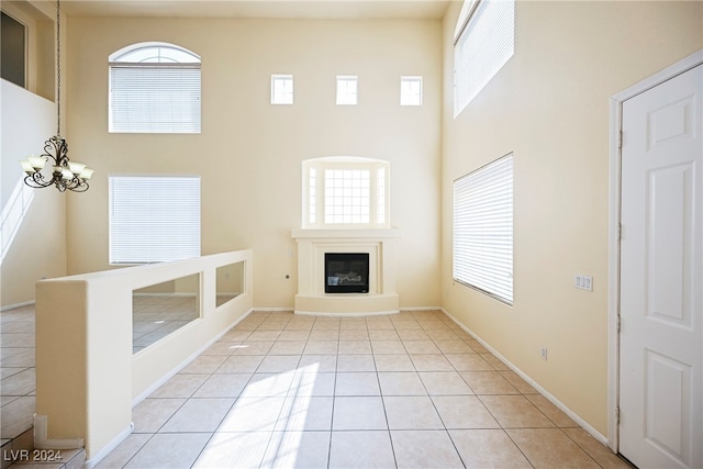 unfurnished living room featuring a high ceiling, plenty of natural light, light tile patterned floors, and a chandelier