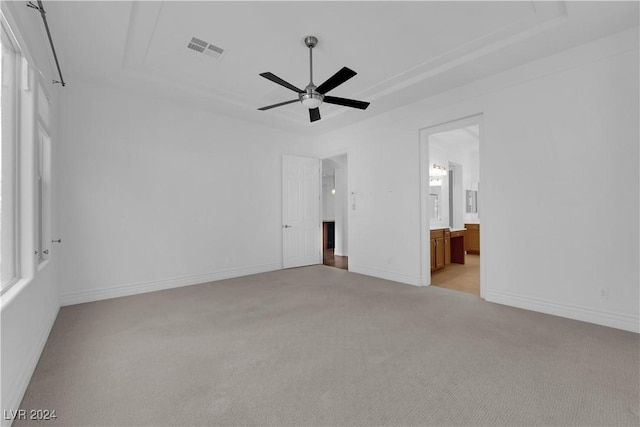 unfurnished bedroom with a tray ceiling, visible vents, light carpet, and baseboards