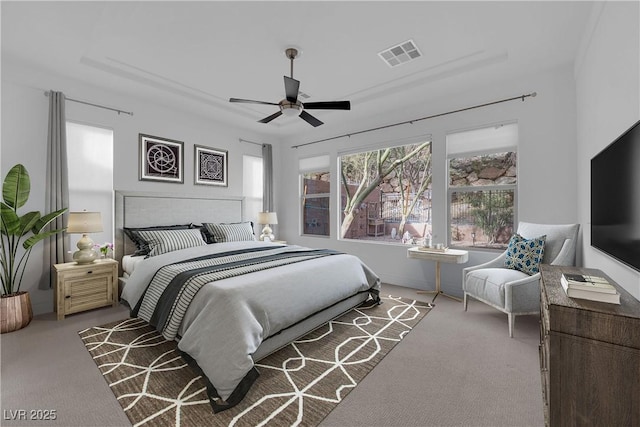 carpeted bedroom with visible vents, a raised ceiling, and ceiling fan