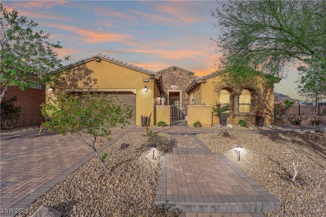 view of front facade featuring decorative driveway, stone siding, a fenced front yard, and stucco siding