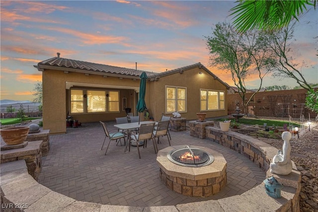 patio terrace at dusk with outdoor dining space, a fire pit, and fence