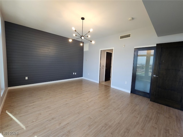 empty room featuring wooden walls, a chandelier, and light hardwood / wood-style floors