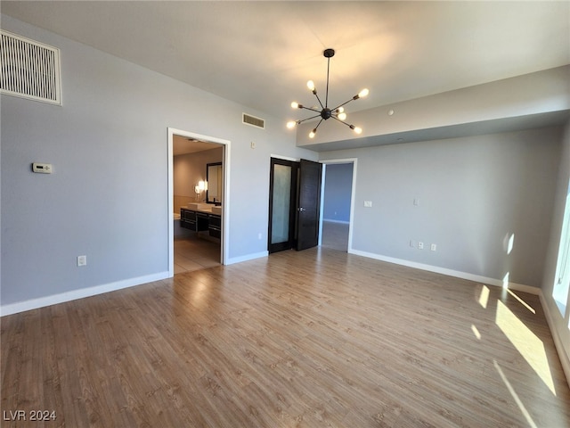 unfurnished bedroom featuring connected bathroom, light hardwood / wood-style flooring, and a notable chandelier