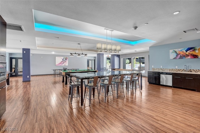 dining room featuring a textured ceiling, a tray ceiling, sink, and light hardwood / wood-style flooring