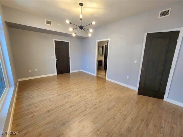 empty room with light hardwood / wood-style floors and a chandelier