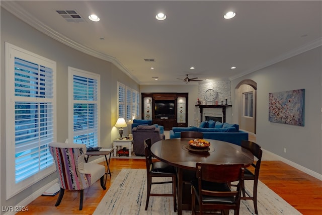 dining room with light hardwood / wood-style floors, ornamental molding, a large fireplace, and ceiling fan