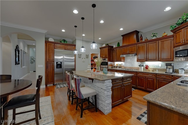 kitchen with light hardwood / wood-style floors, a kitchen island, built in appliances, crown molding, and decorative light fixtures