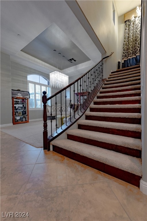 stairway featuring tile patterned flooring, a tray ceiling, and a chandelier