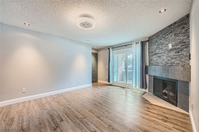 unfurnished living room with light wood-type flooring, a tiled fireplace, and a textured ceiling