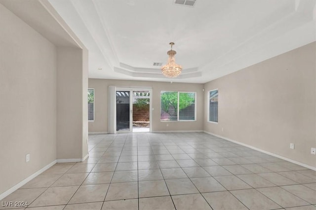 spare room with light tile patterned floors, a tray ceiling, baseboards, a notable chandelier, and visible vents