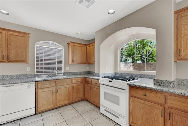 kitchen with a sink, light tile patterned flooring, visible vents, white appliances, and light stone countertops