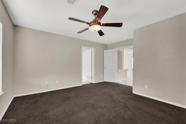 empty room featuring dark colored carpet, visible vents, a ceiling fan, and baseboards
