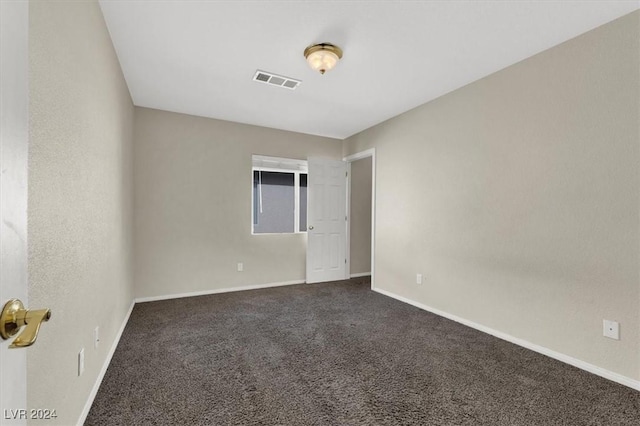 spare room featuring baseboards, dark colored carpet, and visible vents