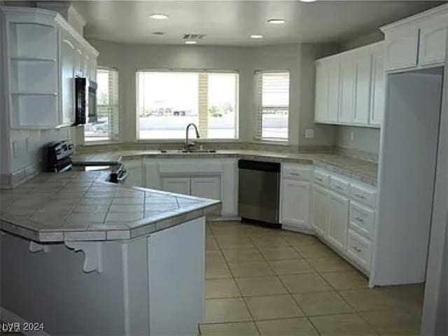 kitchen featuring stainless steel appliances, tile counters, a healthy amount of sunlight, and white cabinetry