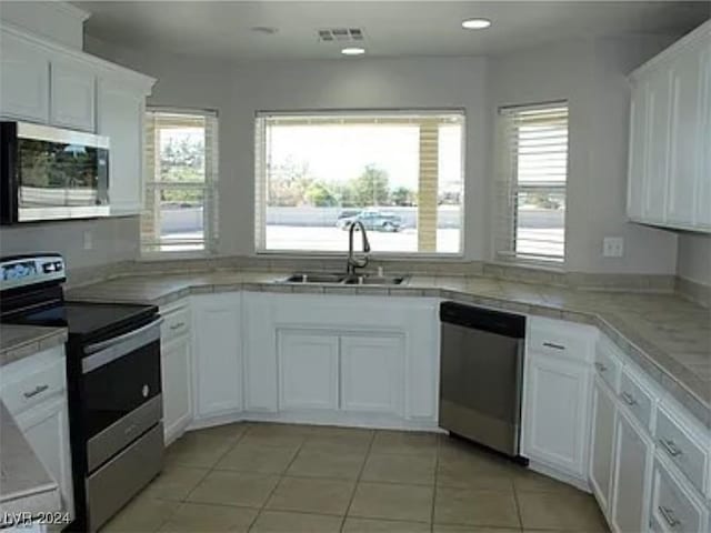 kitchen with appliances with stainless steel finishes, sink, light tile patterned floors, and white cabinets