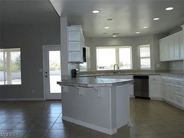 kitchen with dark tile patterned flooring, white cabinets, a kitchen breakfast bar, tile countertops, and stainless steel dishwasher