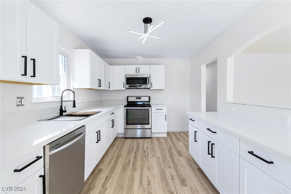 kitchen featuring appliances with stainless steel finishes, light wood-type flooring, sink, and white cabinets