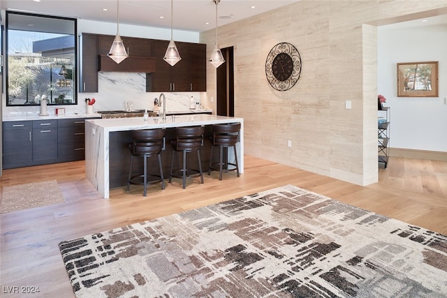 kitchen with a kitchen bar, a kitchen island with sink, dark brown cabinets, and light hardwood / wood-style flooring