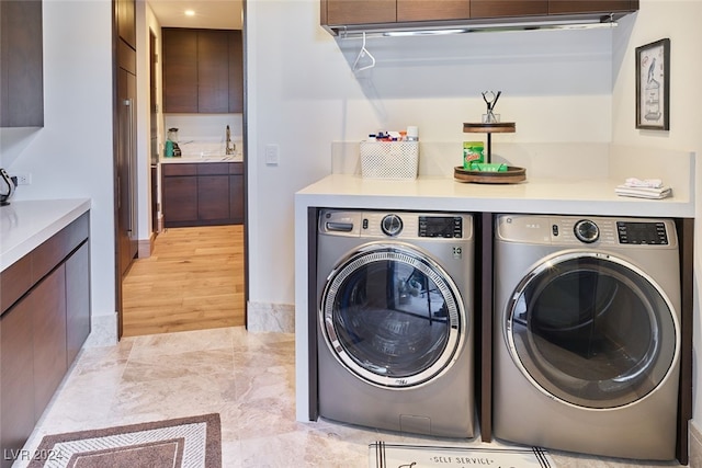 clothes washing area featuring separate washer and dryer, cabinets, light hardwood / wood-style flooring, and sink