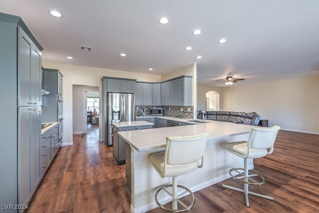 kitchen featuring kitchen peninsula, stainless steel refrigerator with ice dispenser, dark hardwood / wood-style flooring, sink, and a breakfast bar area