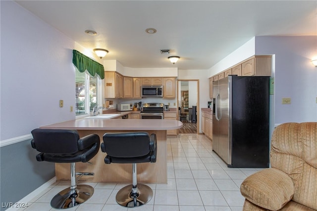 kitchen featuring sink, kitchen peninsula, a kitchen bar, stainless steel appliances, and light tile patterned floors