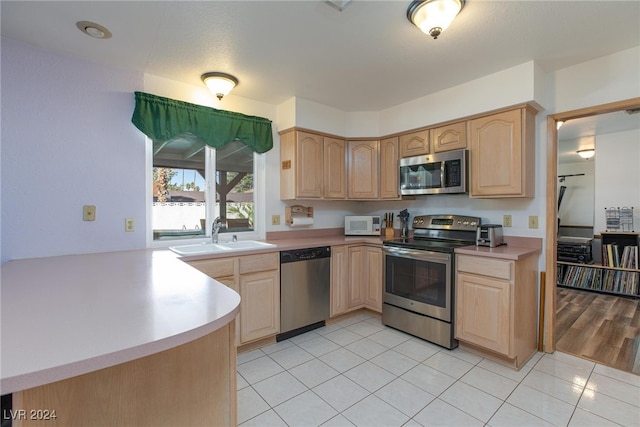 kitchen with light brown cabinets, stainless steel appliances, sink, and kitchen peninsula