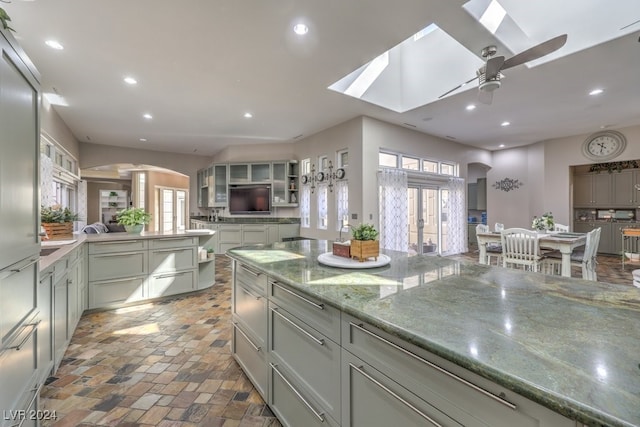 kitchen with arched walkways, a ceiling fan, recessed lighting, gray cabinetry, and light stone counters