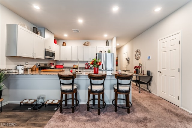 kitchen with kitchen peninsula, dark wood-type flooring, white cabinetry, stainless steel appliances, and a breakfast bar