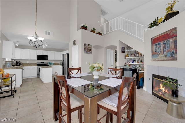 dining space featuring an inviting chandelier, a towering ceiling, a tile fireplace, and light tile patterned flooring